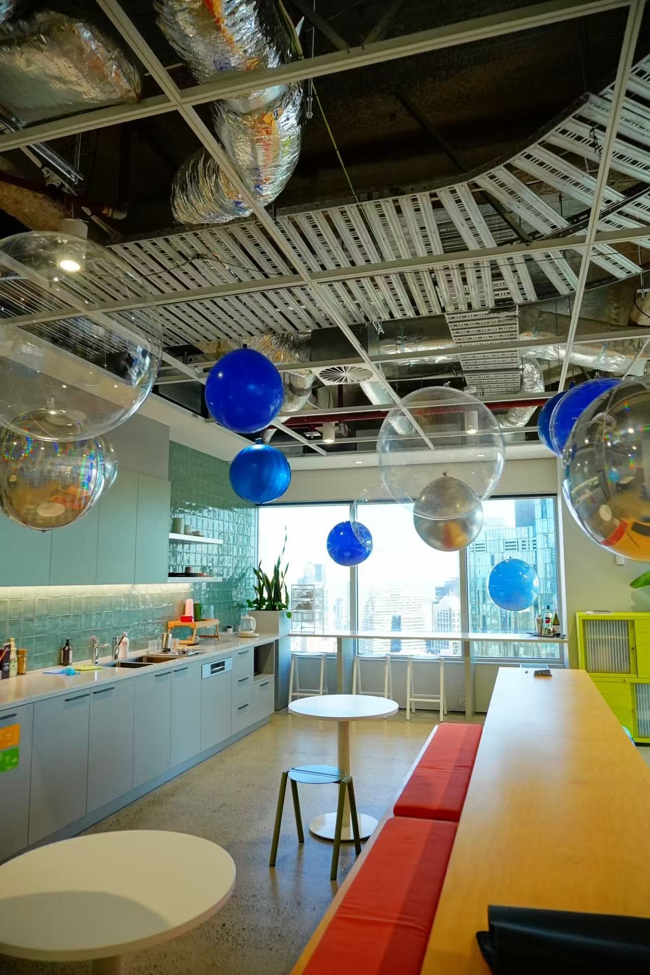 Contemporary office space celebration featuring suspended transparent and blue balloons, creating an elegant floating effect against industrial ceiling design. Perfect for corporate events, office openings, or modern workspace celebrations.