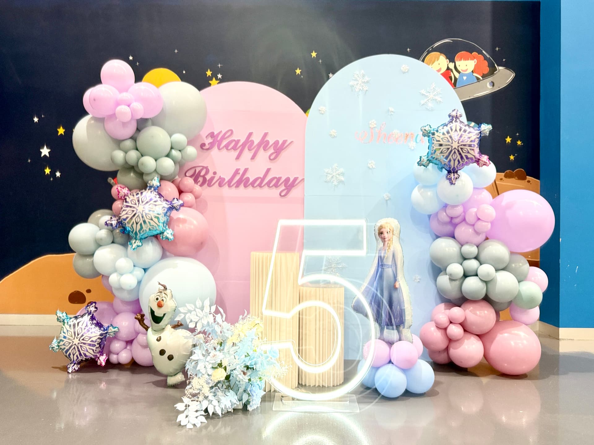 Happy Birthday 5th celebration with pink and light blue backdrop, illuminated number 5 and pastel balloon garlands