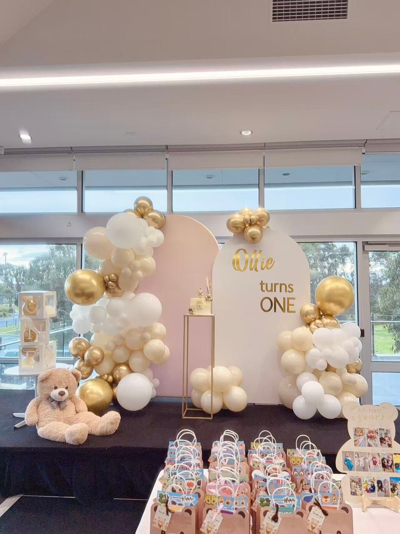 White and gold 1st birthday with teddy bear, arch backdrops and organic balloon garlands.