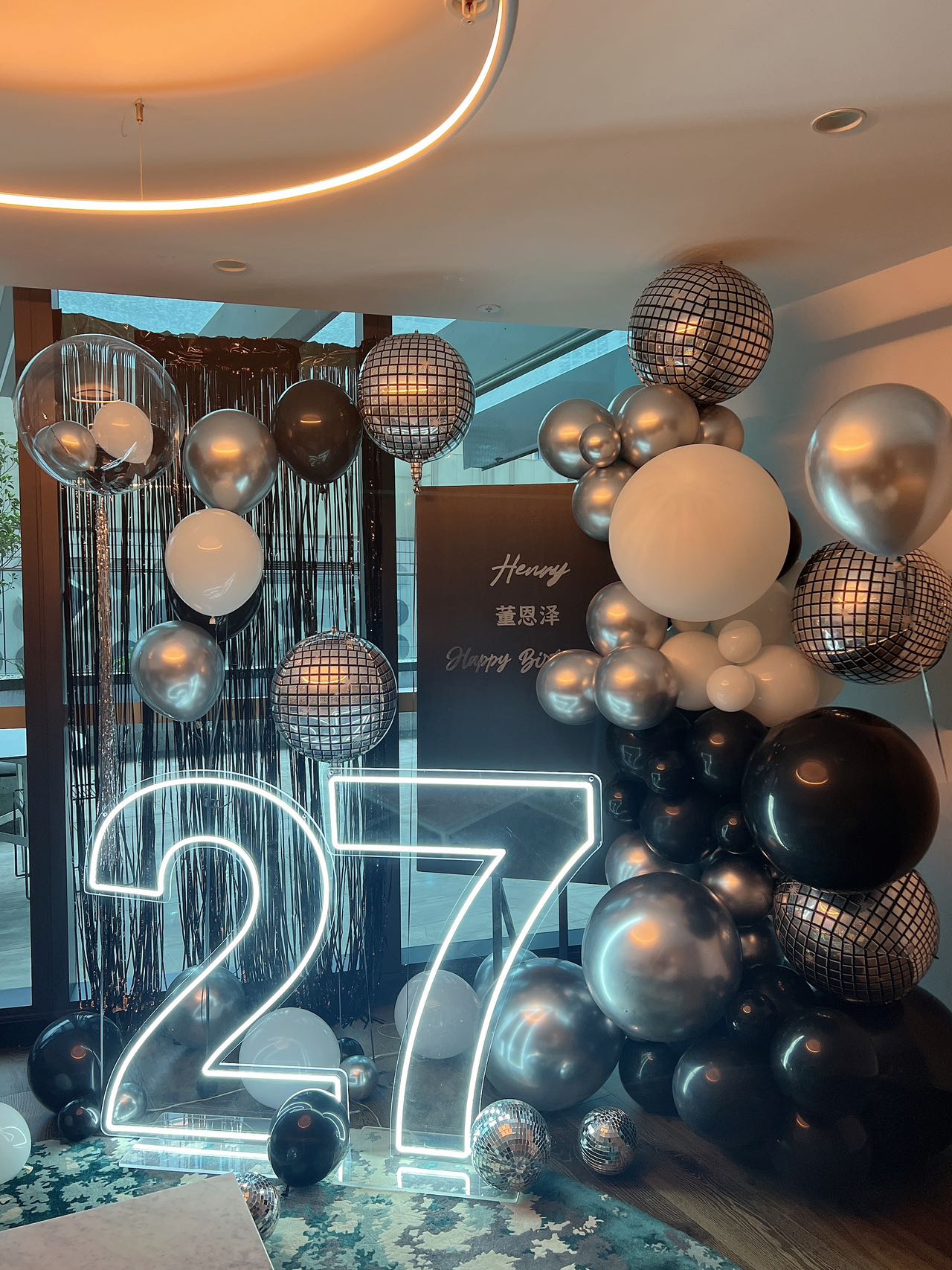 Modern 27th birthday celebration with neon number lights, disco balls and silver-black balloon arrangement