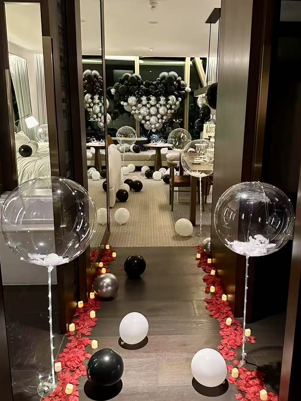 Sophisticated black and white proposal setup with heart-shaped balloon backdrop, transparent bubble balloons, and romantic candlelit pathway with rose petals. Perfect for anniversaries, proposals, and elegant adult celebrations.