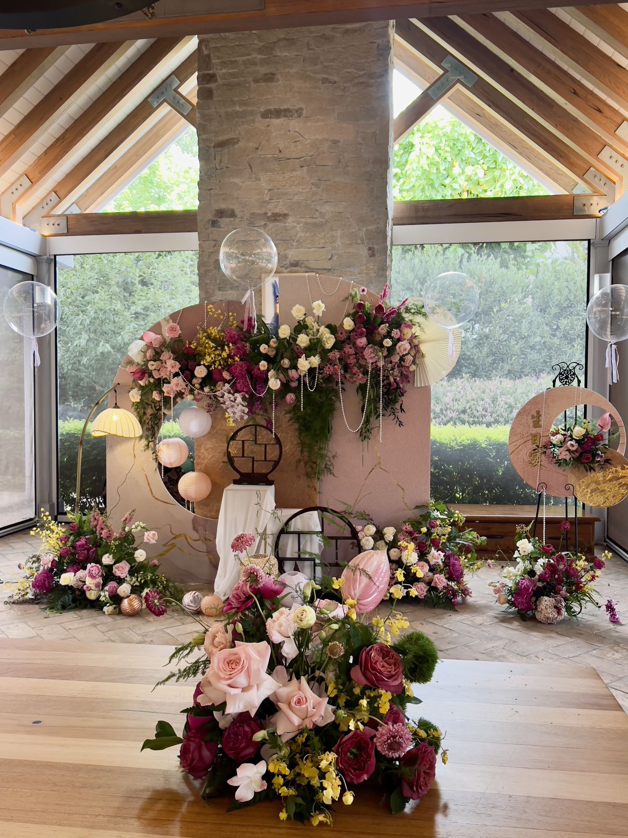 Enchanting garden room birthday setup with luxurious floral arrangements in pink and burgundy, transparent balloons and vintage decor