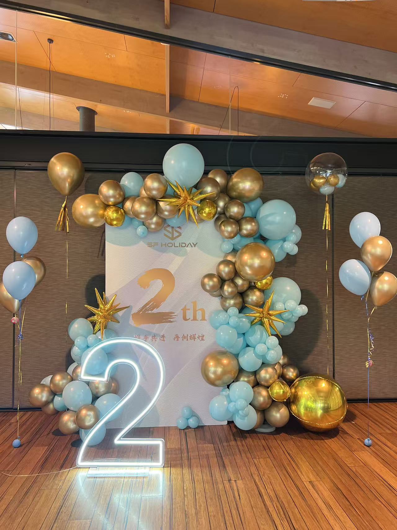 Modern 2nd anniversary celebration with LED number light, mint blue and chrome gold balloon garland, and star decorations