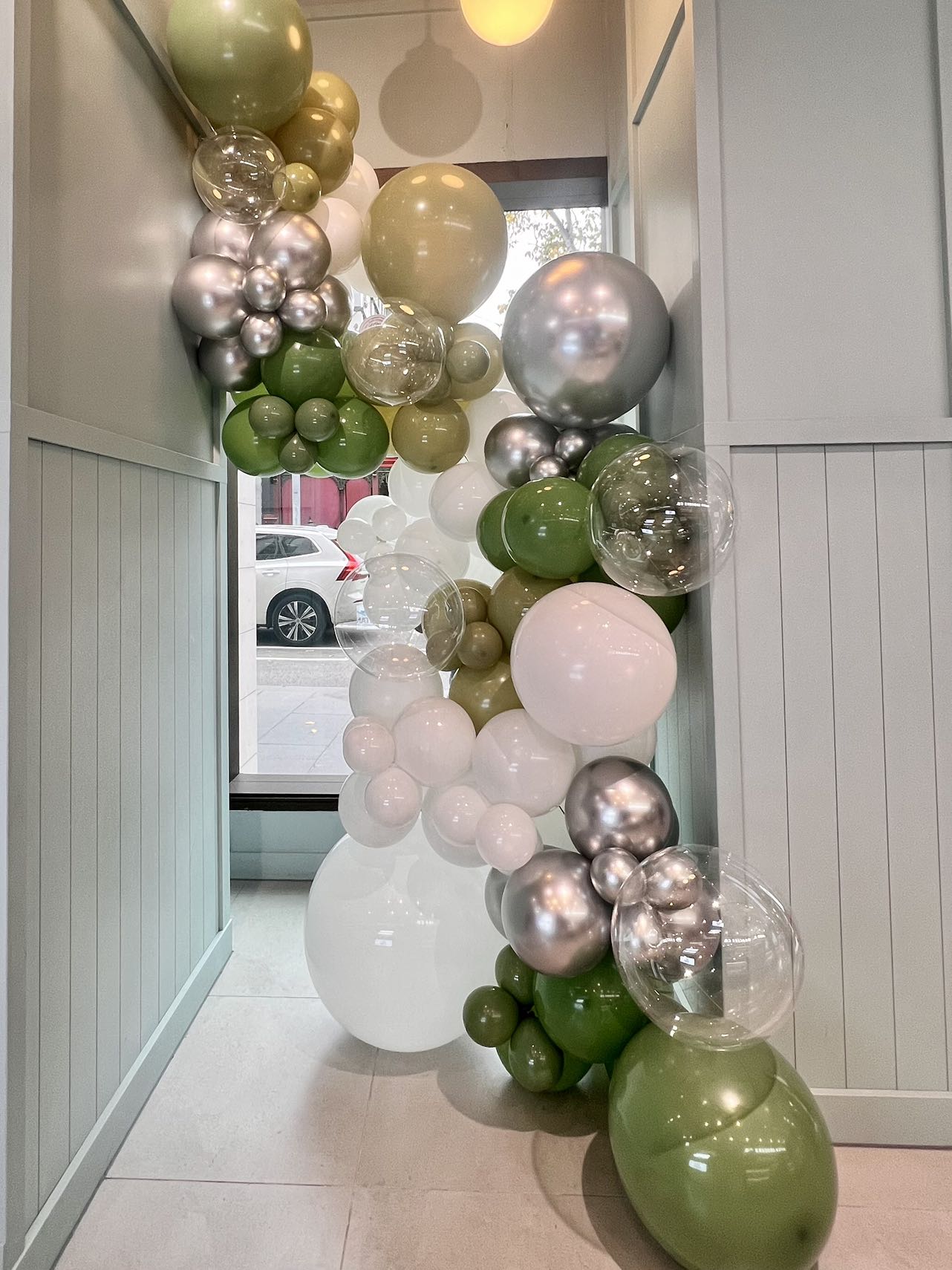 Modern cafe entrance with elegant olive green, chrome and white organic balloon installation