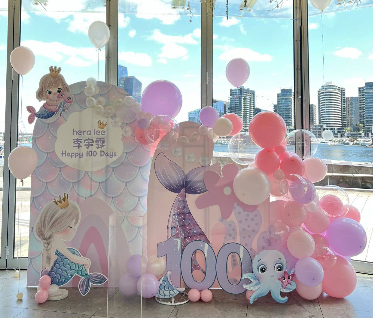 Sweet mermaid themed 100 days celebration with pink and purple balloons by the harbor