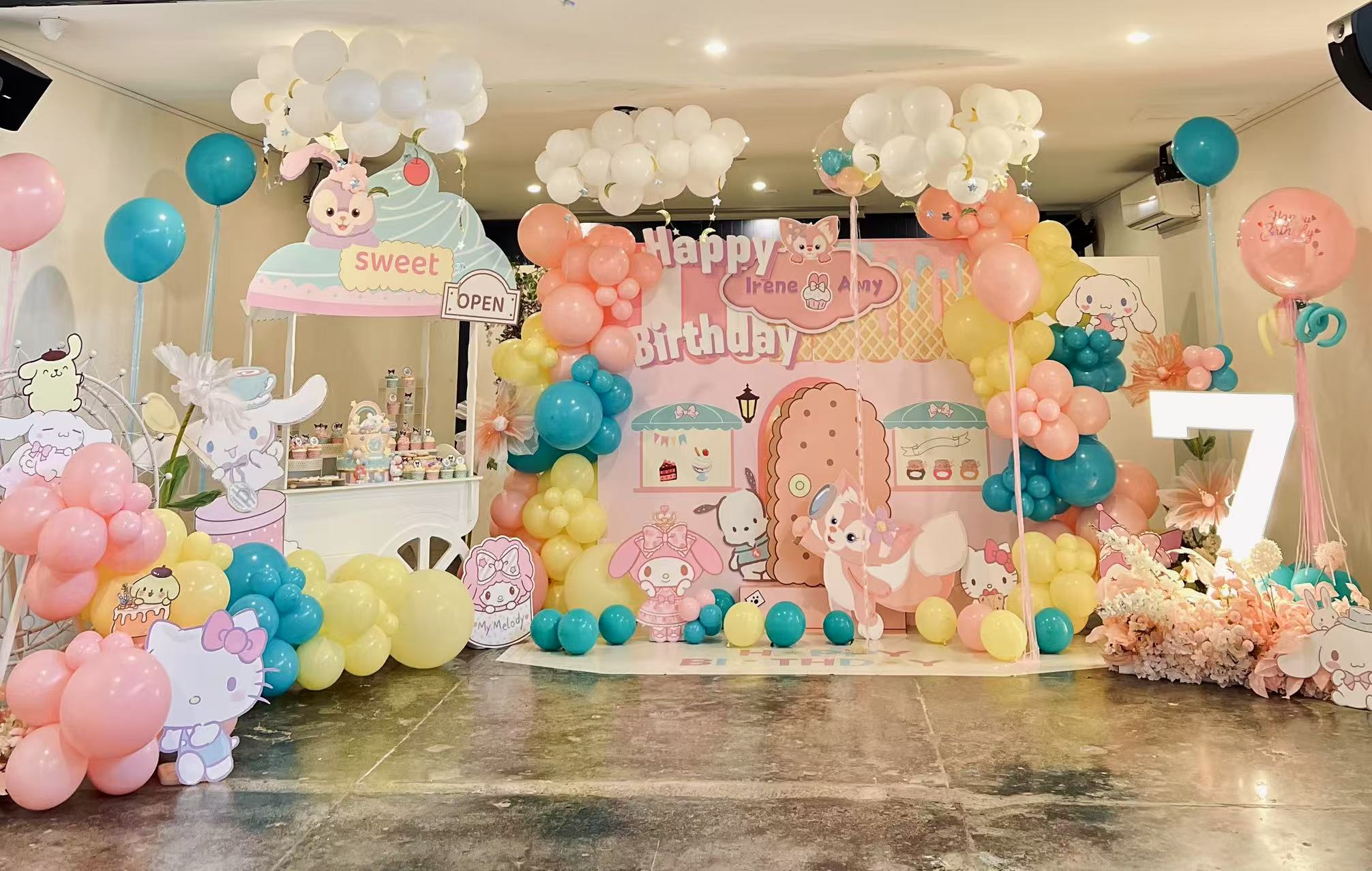 Sweet pastel birthday party with pink, blue and yellow balloon garland, featuring cute cartoon characters and cloud decorations