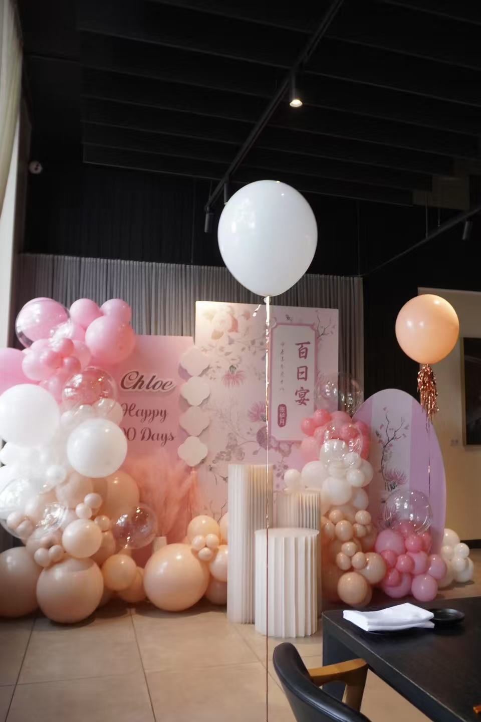 Elegant pink and white 100 days celebration for Chloe featuring a custom backdrop with cherry blossom design and Chinese characters. Beautiful pastel pink organic balloon arrangement with peach accents, complemented by suspended white helium balloons creating a dreamy atmosphere.