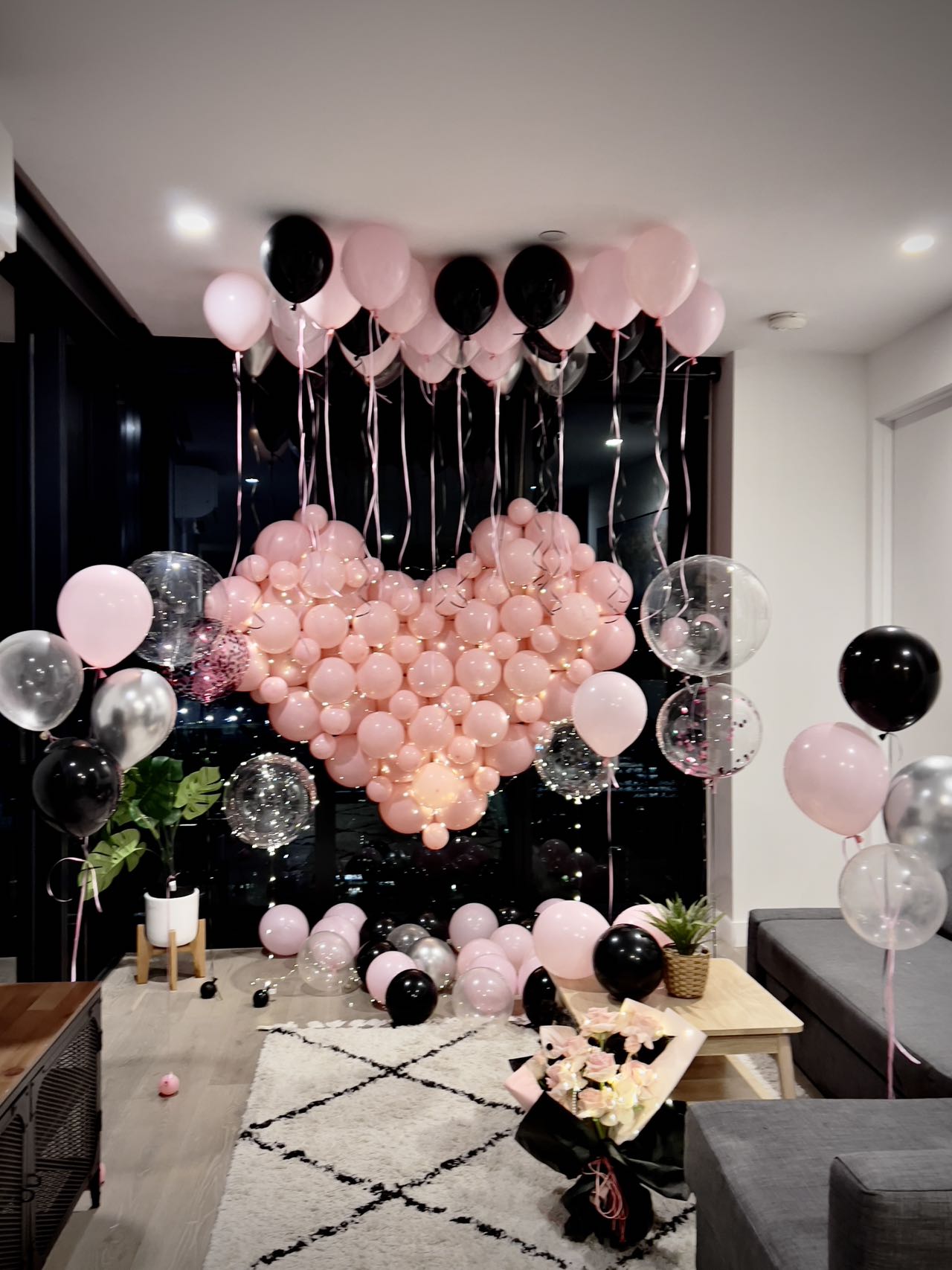 Romantic proposal setup with pink heart-shaped balloon wall and black accents