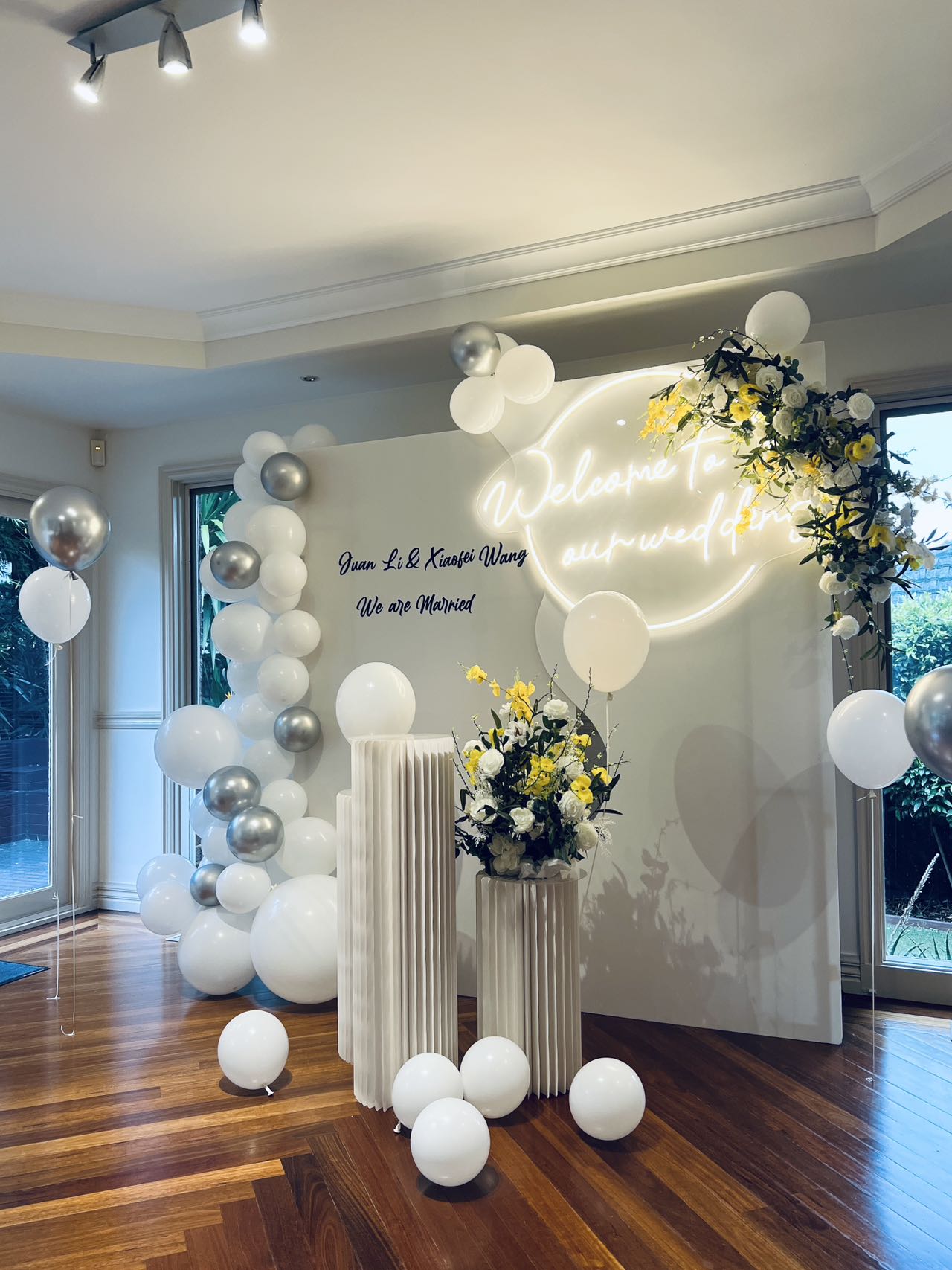 Modern wedding setup with neon sign, white and silver balloons, and yellow floral accents